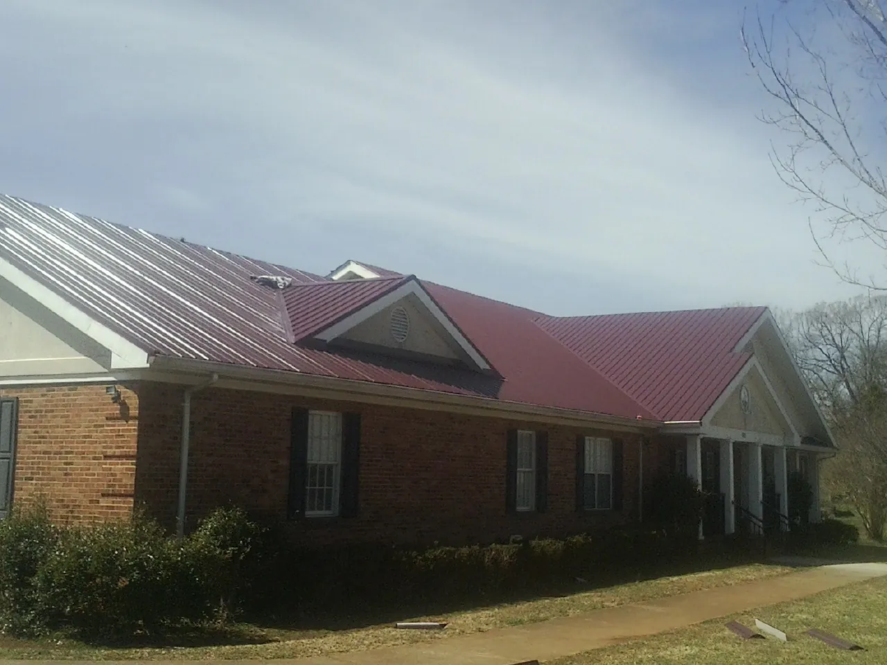 Red metal roof with gabled entries on a long brick building, from a Hail Damage Roof Repair job in Baldwyn