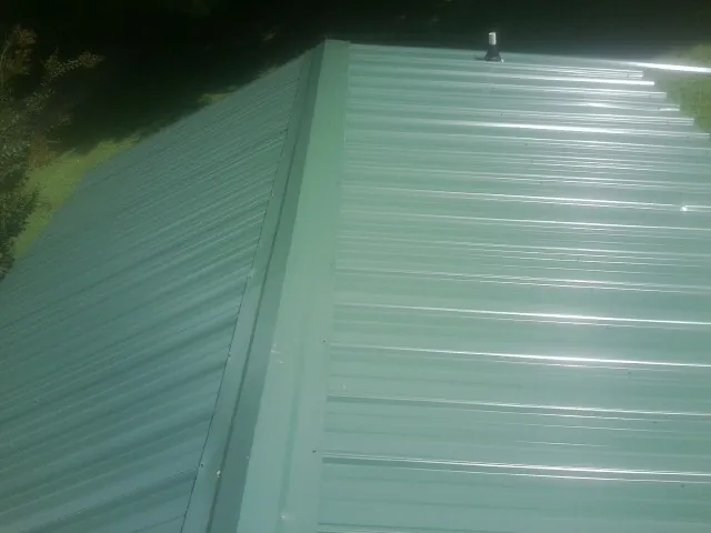 New green metal panels meeting at the ridge of a roof — Flat Roof Repair work by our crew in Baldwyn