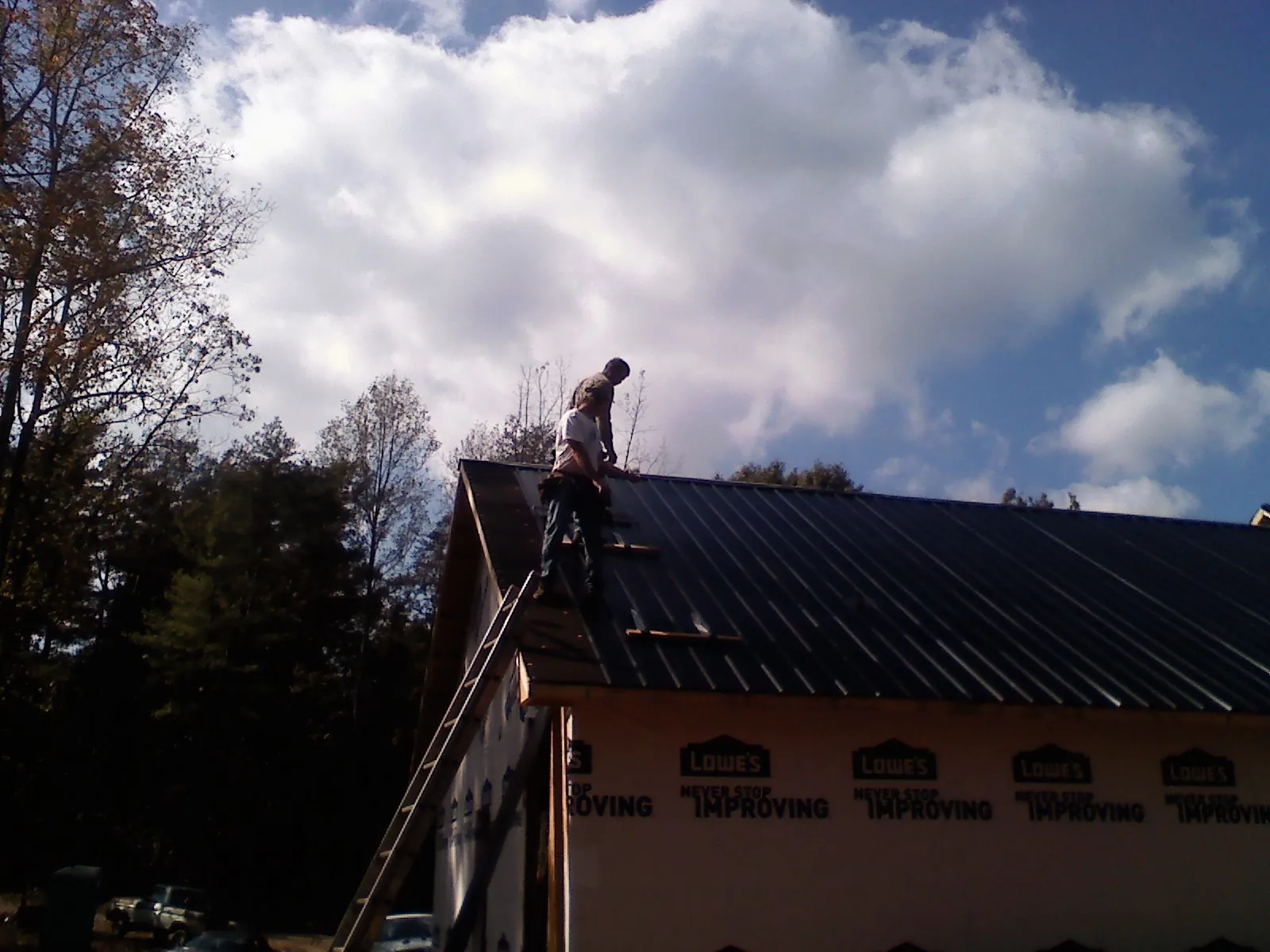 Roofer fastening dark metal panels high against a cloudy sky, from a Roof Inspection job in Baldwyn