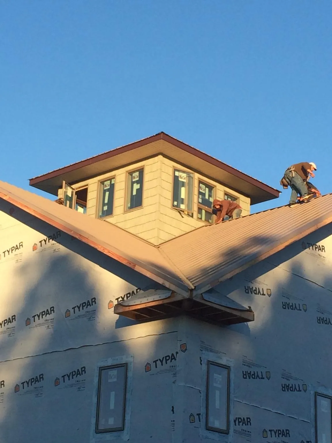 Roofers working around a rooftop cupola on a new metal roof at sunset — Roof Waterproofing in Baldwyn by Roofing Brothers